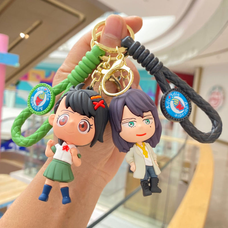 Girl figure keychain with green braided strap and gold-tone clasp