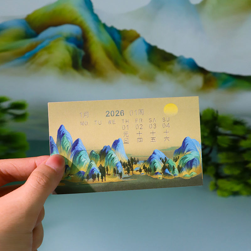 Handheld paper memo calendar featuring colorful mountain landscape artwork