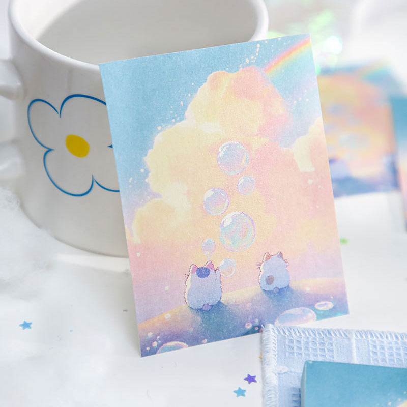 Pastel notebook featuring two bunnies beneath clouds, bubbles, and a rainbow